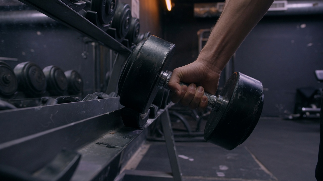 A hand lifting a dumbbell off the rack in a dark gym.